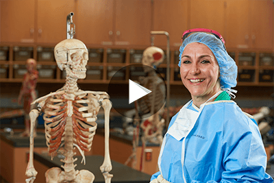 OCC student in surgical scrubs, next to a skeletal model.