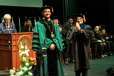 OCC's 9th Chancellor Peter M. Provenzano Jr standing on stage surrounded by staff, faculty, students and the community. 