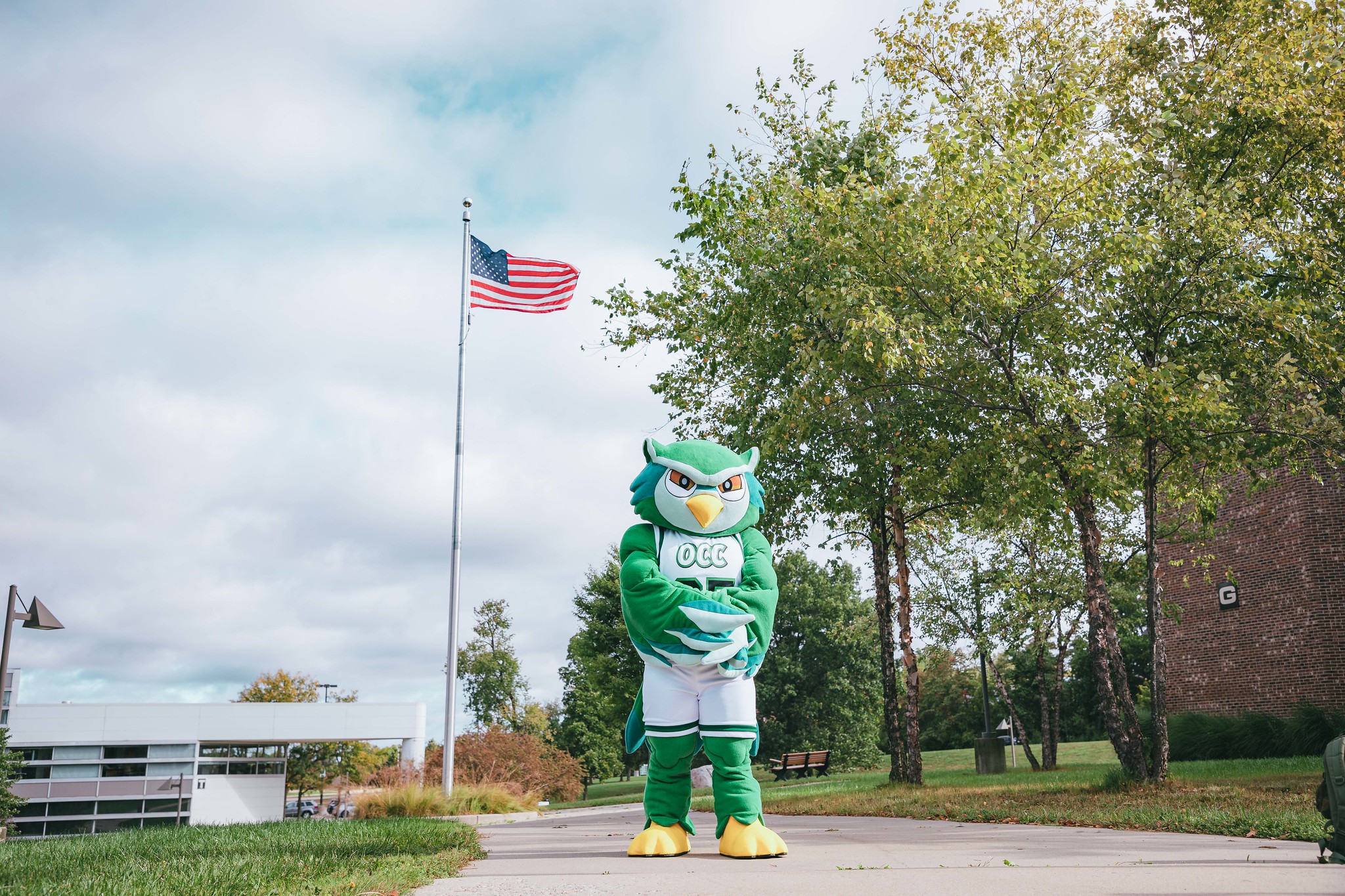 Talon the Owl mascot standing outside by flagpole